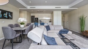Ein modernes Wohnzimmer mit einer Eckcouch, grauen Sesseln, einem Esstisch und einer Küche im Hintergrund.