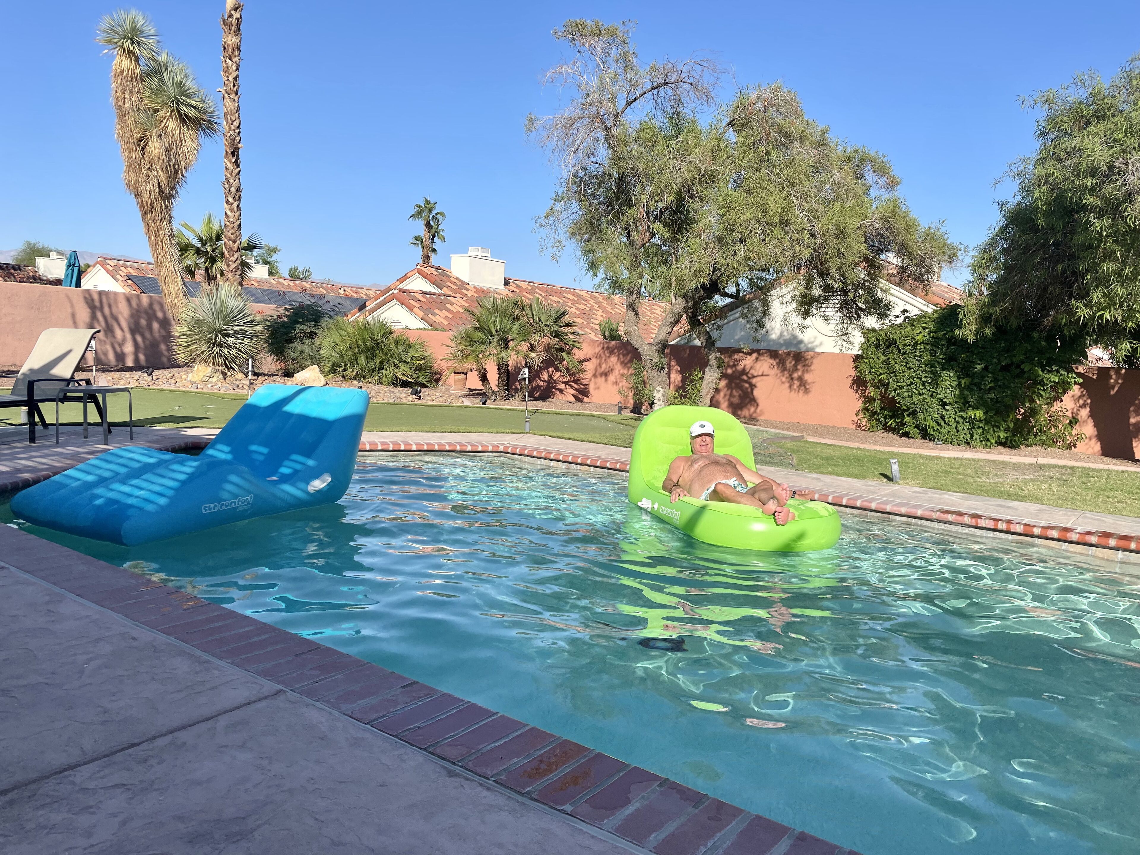 Une piscine avec deux matelas gonflables, un bleu et un vert, et un ciel d’un bleu limpide.
