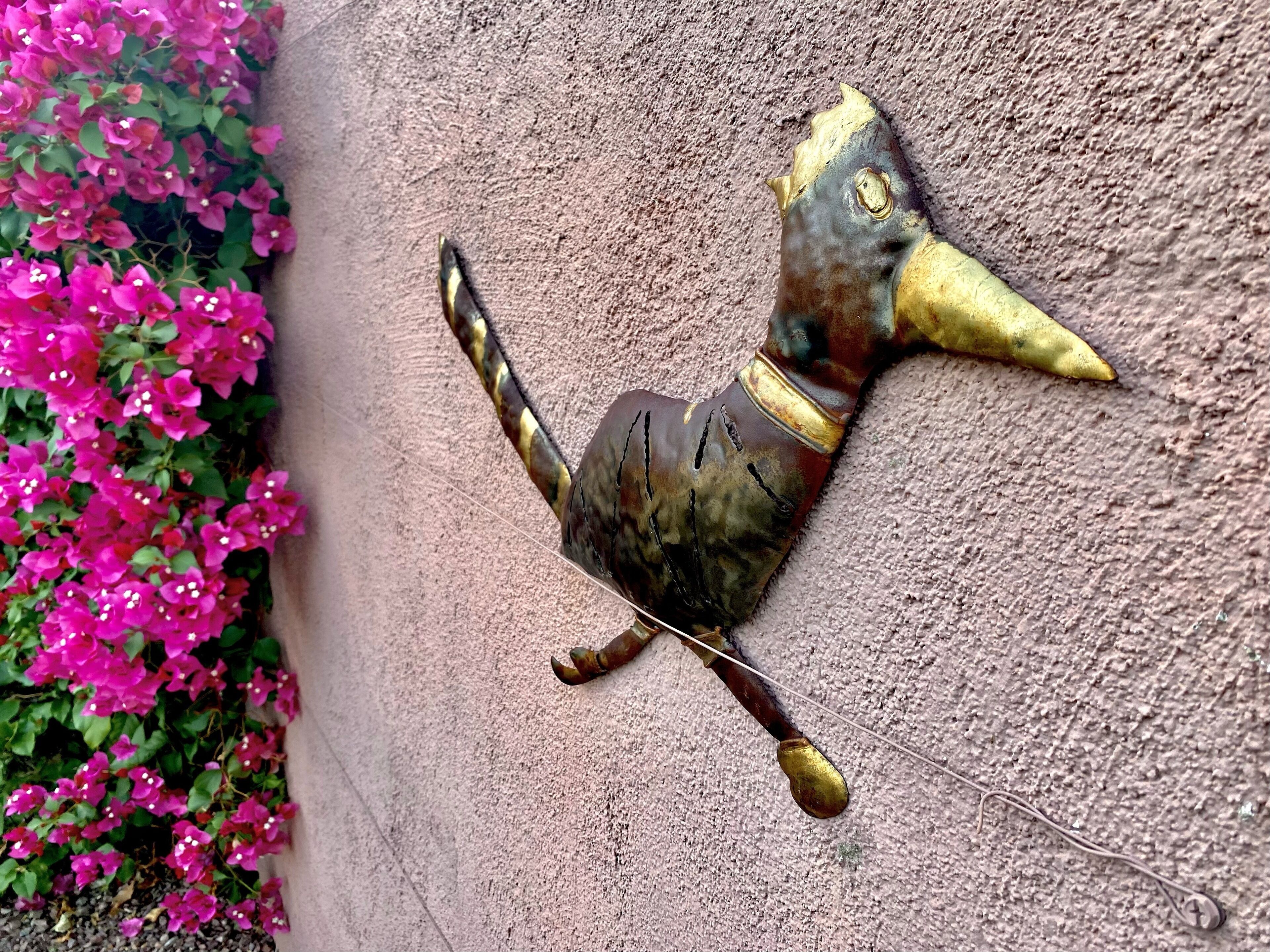 Een aan de muur bevestigd sculptuur van een vogel met een lange snavel en een gebogen staart.