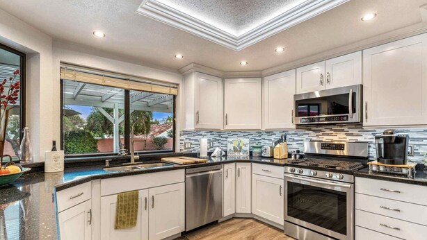 Una cocina moderna con armarios blancos, electrodomésticos de acero inoxidable y un amplio ventanal con vistas a zonas verdes.