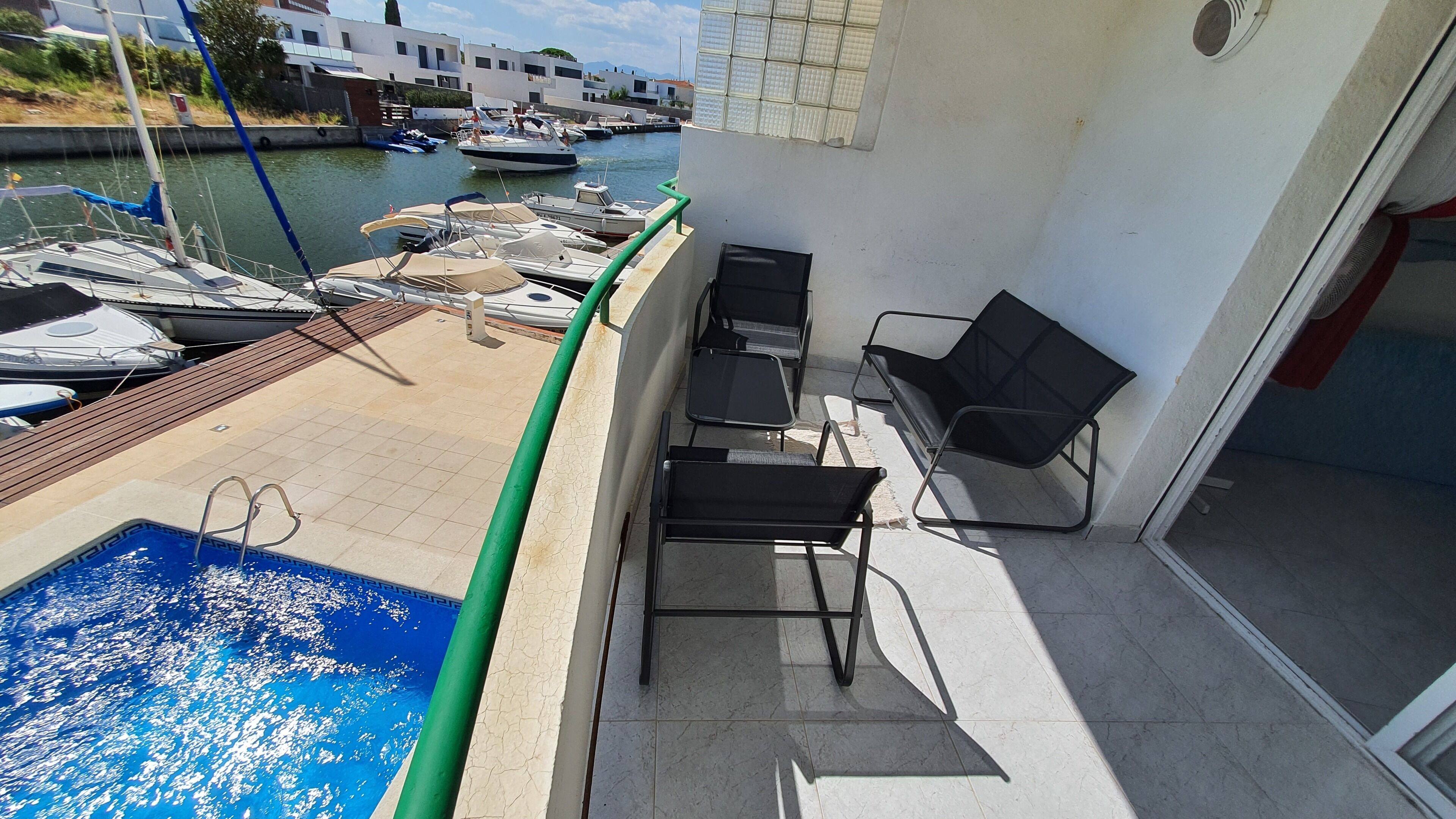 A balcony with a pool, chairs, and a view of boats and buildings.