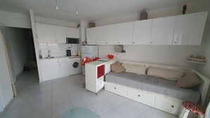 A compact kitchen with a washing machine, a microwave, and a sink. There is a sofa with cushions and a small table with a bowl.