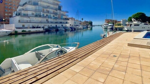 A marina with boats docked, a wooden walkway, and a building with balconies.