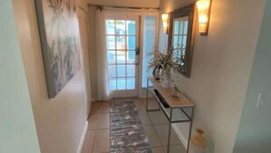 Un pasillo con suelo de baldosas, techo de madera, una puerta con paneles de vidrio y un espejo adosado a la pared.