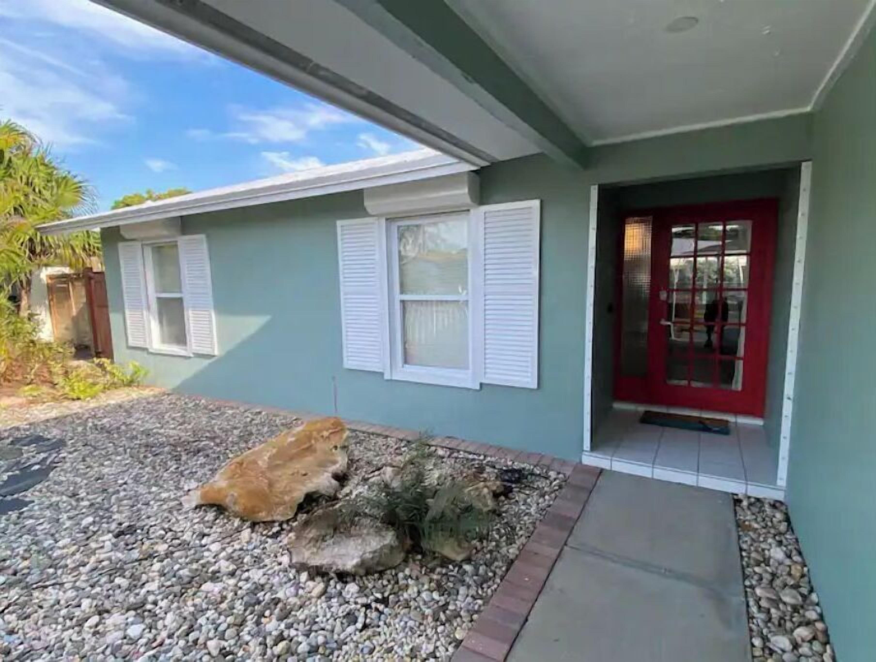 A house with a red door, white shutters, and a gravel driveway.