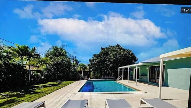 Piscina con sillones de descanso, rodeada de follaje y un edificio con ventanales grandes.