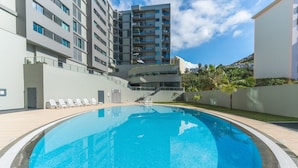 A swimming pool with lounge chairs, a modern building with balconies, and a clear sky. - Terrace Apartment by Atlantic Holiday (Funchal)