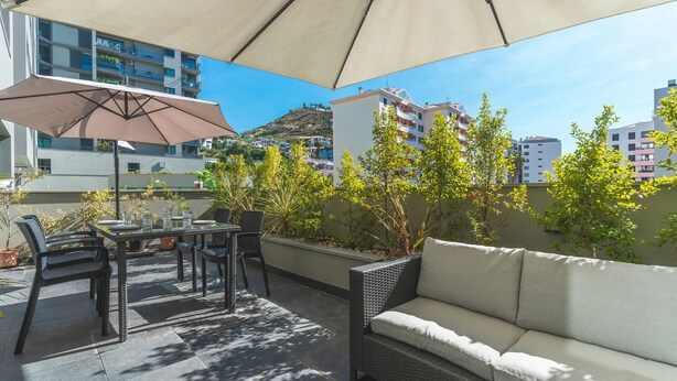 An outdoor patio with a table, chairs, and a sofa under a large umbrella. - Terrace Apartment by Atlantic Holiday (Funchal)