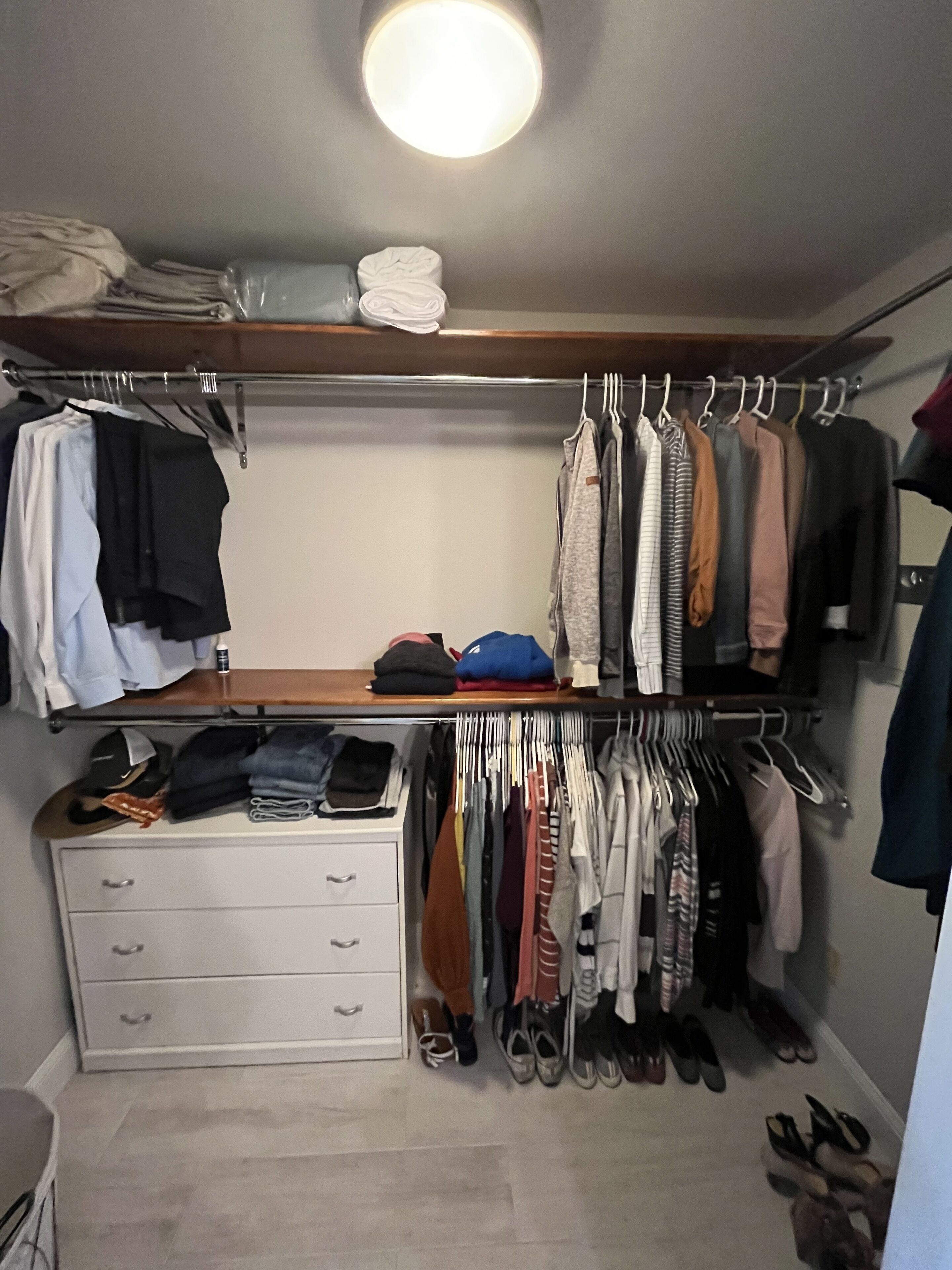 Een inloopkast met hangende kleding, opgevouwen spullen op planken en een schoenenrek.