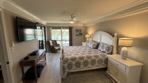 Een slaapkamer met een bed, een televisie, een stoel, een bureau en een raam met uitzicht op een zwembad.