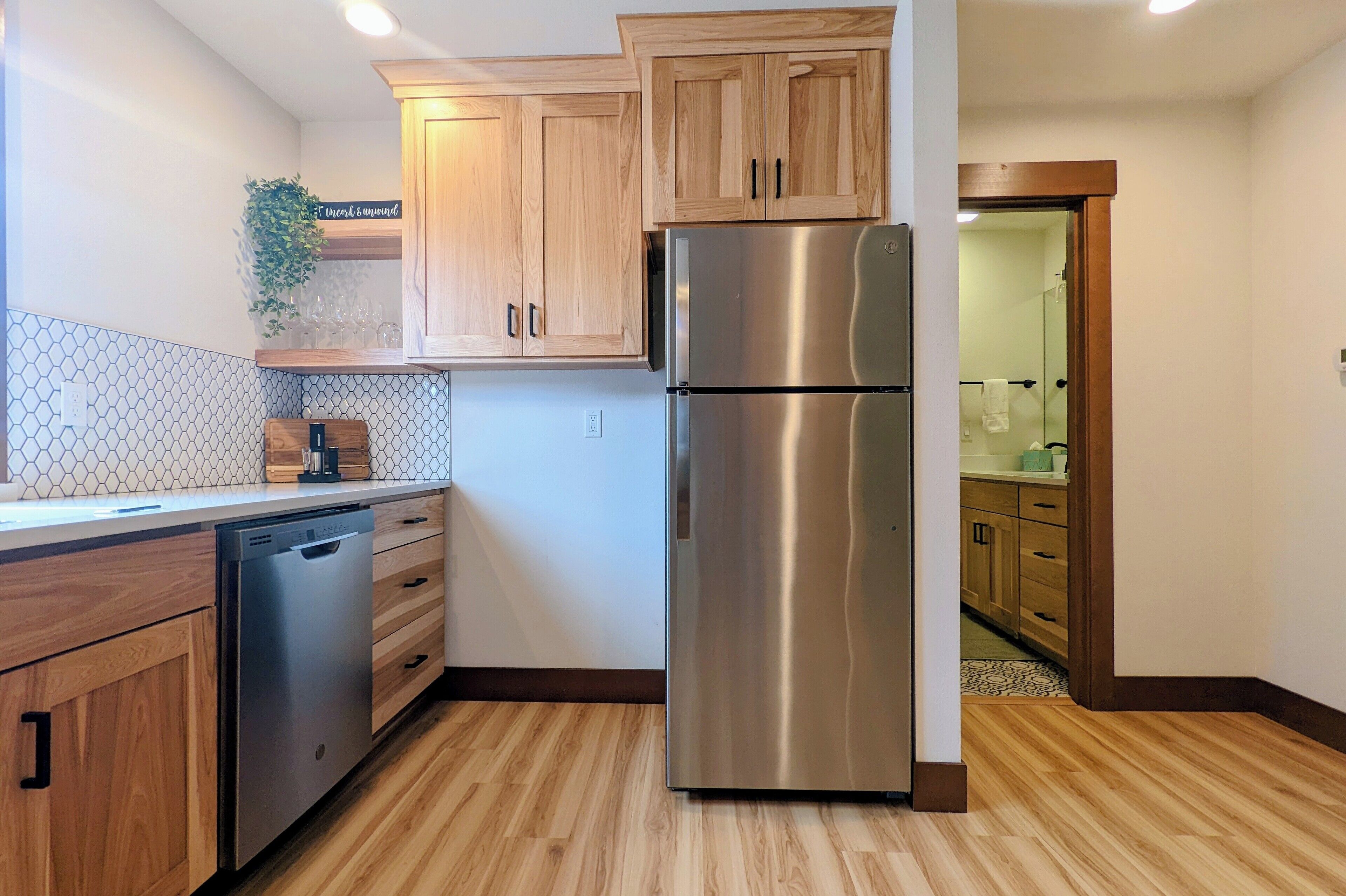 A kitchen with wooden cabinets, a stainless steel refrigerator, a dishwasher, and a countertop with a plant and a coffee maker.