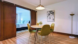 Een moderne kamer met een eettafel, stoelen, een hanglamp en een bed op de achtergrond.