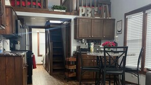 A compact kitchen with wooden cabinets, a dining area with chairs, and a loft bedroom with a red bedspread. - One bedroom  in United States of America, Hutto (Hutto)