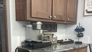 A kitchen with wooden cabinets, a coffee maker, a sign that says "Coffee + Tea + Cocoa", and a sign that says "pour some sugar on me - coffee". - One bedroom  in United States of America, Hutto (Hutto)