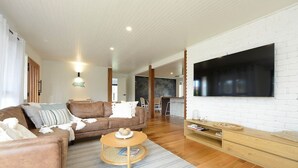 Ein modernes Wohnzimmer mit einem großen Flachbildfernseher, einem braunen Ledersofa, einem runden Couchtisch und einer Holz-TV-Konsole.