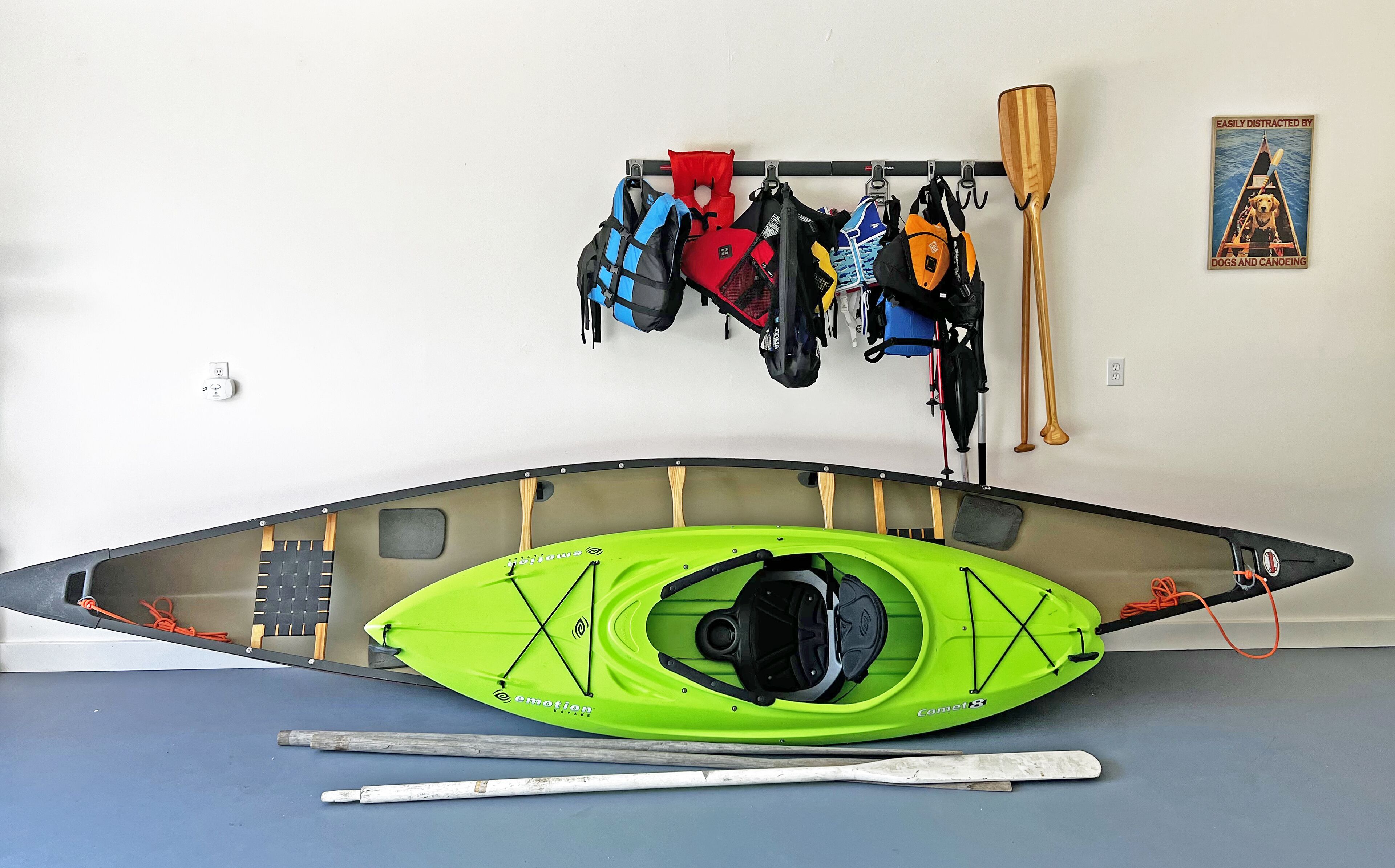 A kayak with a green hull, a paddle, and a life jacket hanging on a wall.