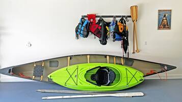 A kayak with a green hull, a paddle, and a life jacket hanging on a wall.