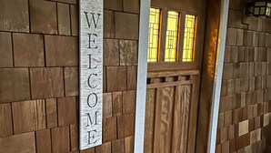 Una puerta de madera con un letrero que dice 'WELCOME' encima, una silla roja y un felpudo con la palabra 'WELCOME'.