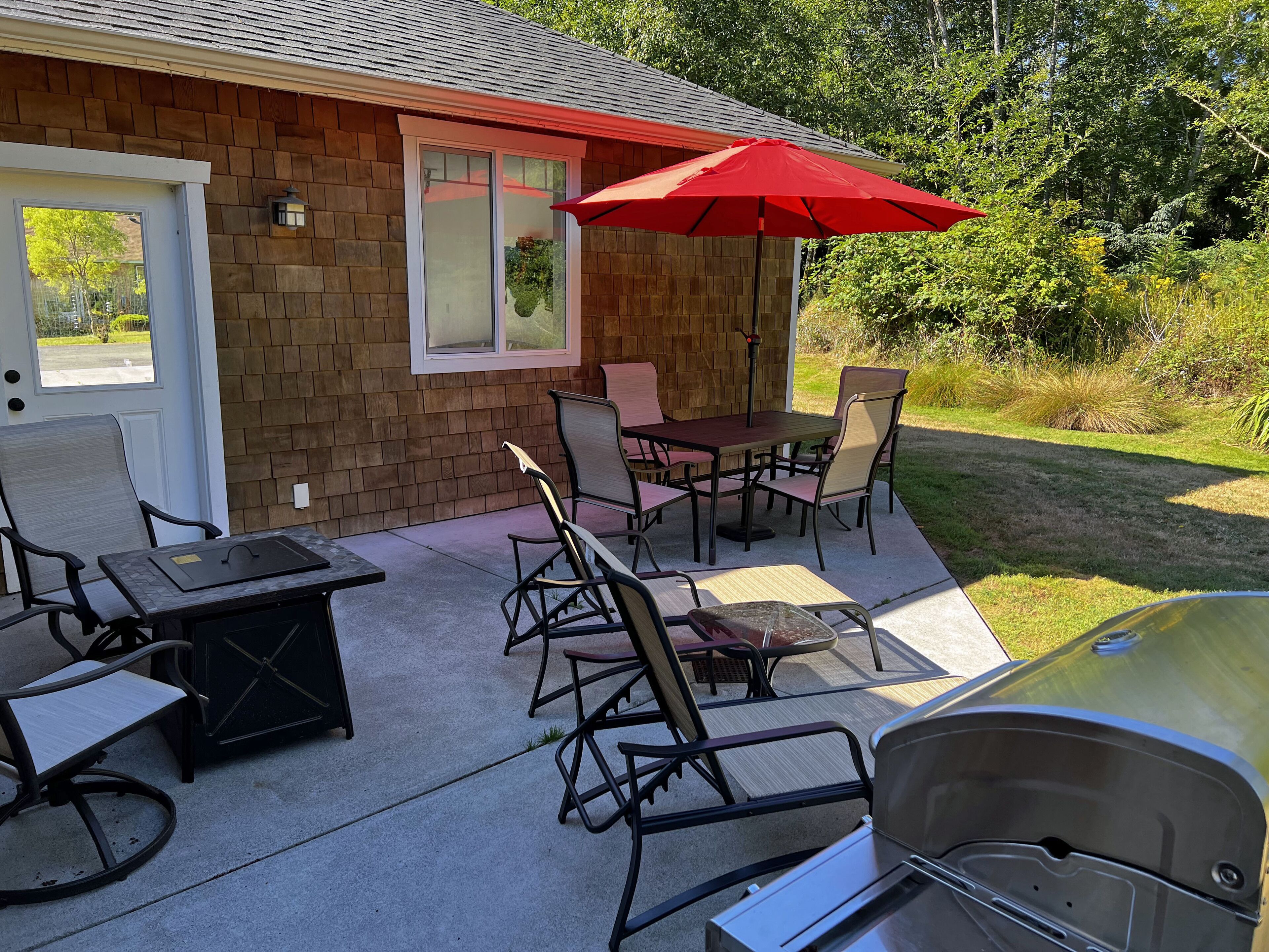 A patio area with a brick wall, a sliding glass door, a red umbrella, and outdoor furniture.