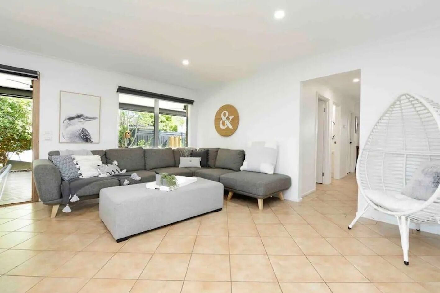 A modern living room with a grey sectional sofa, a white coffee table, and a white hanging chair.
