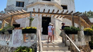 A historic building with a wooden pergola entrance, stone steps, and potted plants.