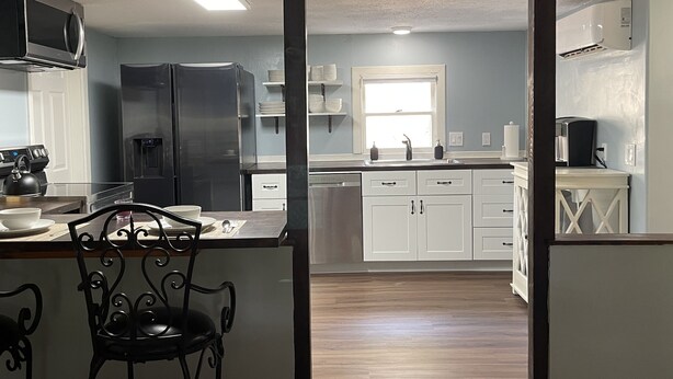 Cocina moderna con refrigerador, microondas y estufa. Hay una zona de comedor con una silla y una mesa.