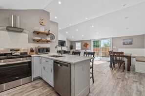 Een moderne keuken met een centraal eiland, roestvrijstalen apparatuur en een eethoek met een houten tafel en stoelen.