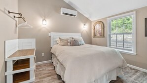 Un dormitorio con cama, mesita de noche, aire acondicionado instalado en la pared y ventana con persianas.