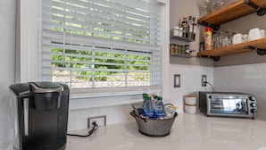 Una cocina con cafetera, tostador y ventana con persianas.
