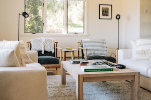 Ein gemütliches Wohnzimmer mit einer Couch, einem Sessel und einem Couchtisch mit Büchern und einer Kamera.