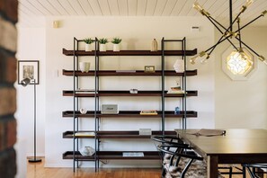 Ein modernes Interieur mit Holzboden, einem Esstisch mit Stühlen, einer an der Wand befestigten Regaleinrichtung mit Dekorationen und einer ungewöhnlichen sechseckigen Leuchte.