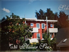 A red building with white windows and balconies, surrounded by trees and greenery. - Apartment (Zislow)