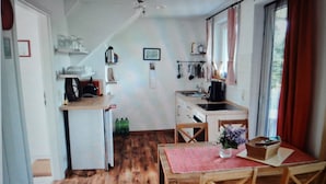 A compact kitchen with wooden flooring, a dining table with chairs, and a window with curtains. - Apartment (Zislow)