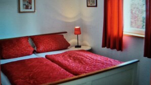 A room with a bed, a lamp, and a window with curtains. - Apartment (Zislow)