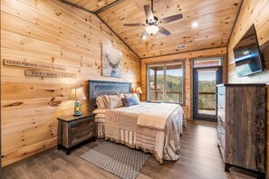 A cozy bedroom with a wooden ceiling, a bed with multiple pillows, a nightstand with a lamp, and a dresser.