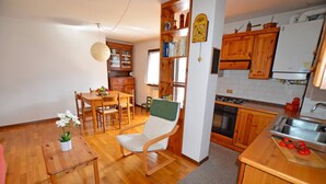 Una cocina con armarios de madera, una zona de comedor con mesa y sillas, y una mesita auxiliar con una planta.