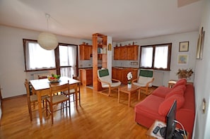 Un coin repas avec une table et des chaises, une cuisine avec des meubles en bois et un canapé rouge avec un téléviseur.