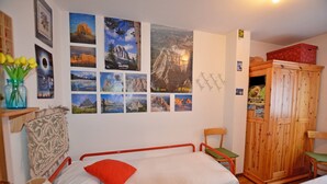 Una habitación con dos camas, un armario de madera, una pared con varias fotografías de paisajes y un jarrón con flores amarillas.