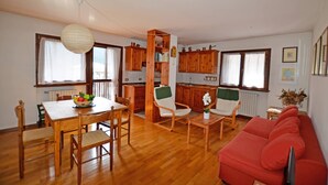 Amplia sala de estar con una mesa de comedor, sillas de madera, un sofá rojo y una cocina con armarios de madera y un ventanal.