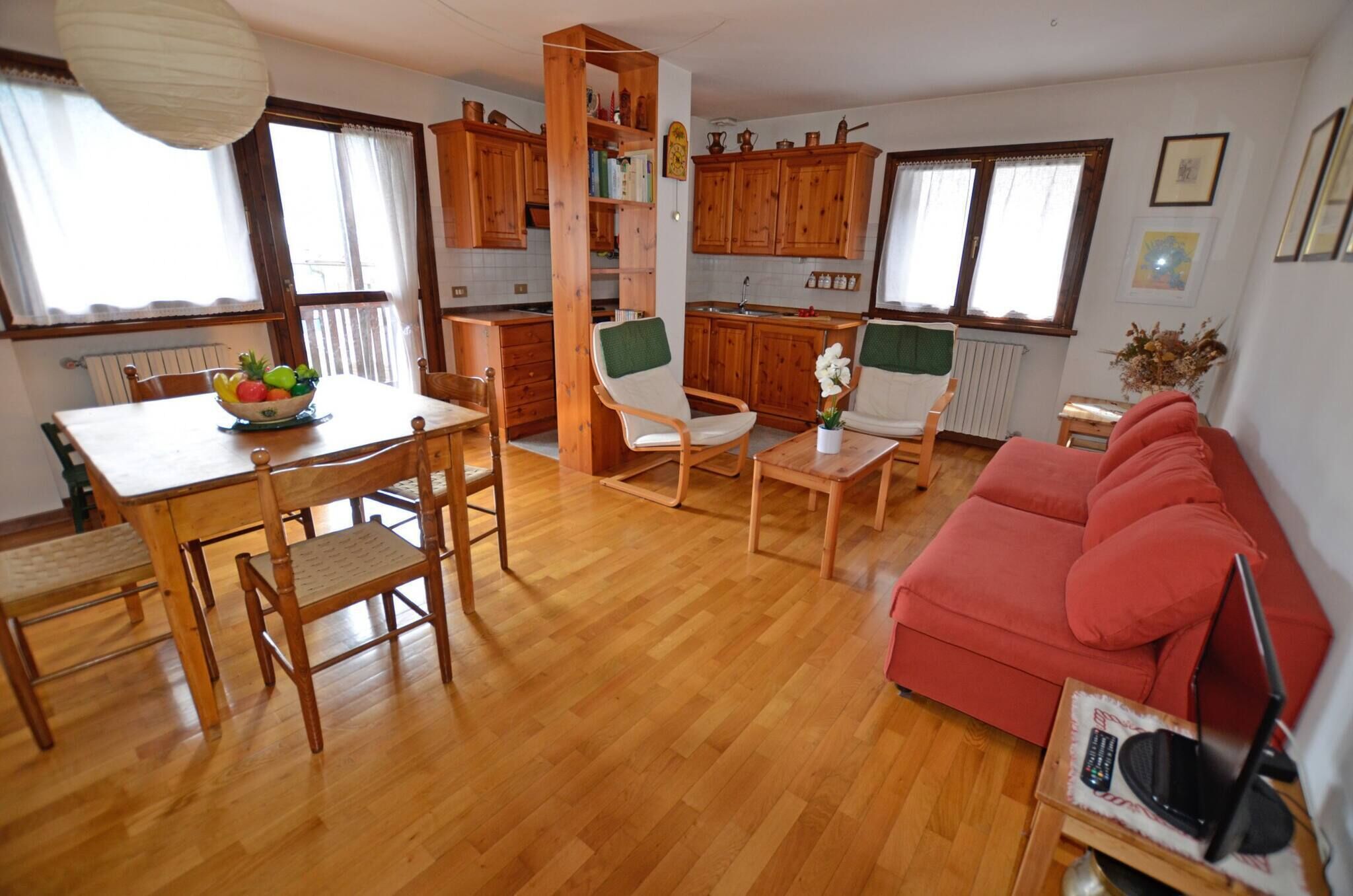 Ein Wohnzimmer mit Esstisch aus Holz, Stühlen, einem roten Sofa und einer Küchenzeile mit Holzausbau.