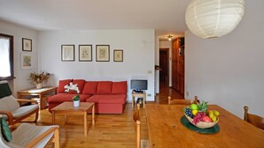 Una sala de estar con un sofá rojo, muebles de madera, un televisor y un frutero sobre una mesa.