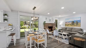 Una sala de estar moderna con comedor, chimenea y un amplio ventanal con vistas a un jardín.