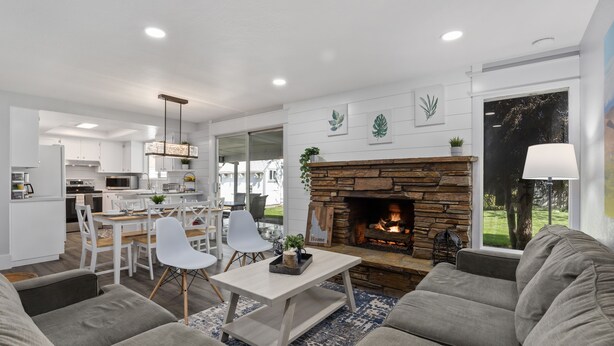 Una sala de estar moderna con chimenea, sofás grises, un comedor y una cocina al fondo.