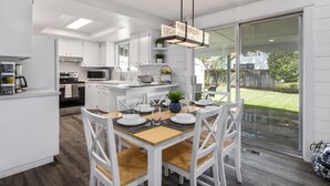 Una cocina moderna con armarios blancos, una mesa de comedor de madera y un amplio ventanal corredera que da a un jardín.