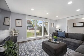 A modern living room with a grey sofa, a coffee table with a plant, and a patterned rug.