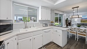 Una cocina moderna con armarios blancos, un microondas integrado, un fregadero y un comedor con mesa y sillas.