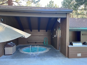 Un área de piscina exterior cubierta con un jacuzzi, un banco y un bote de basura.