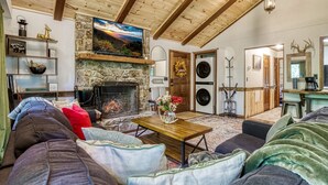Un salon chaleureux avec une cheminée en pierre, un téléviseur fixé au-dessus et un plafond en bois rustique.