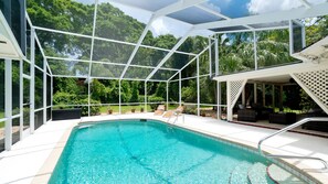 A swimming pool with a glass enclosure, surrounded by outdoor furniture and lush greenery.