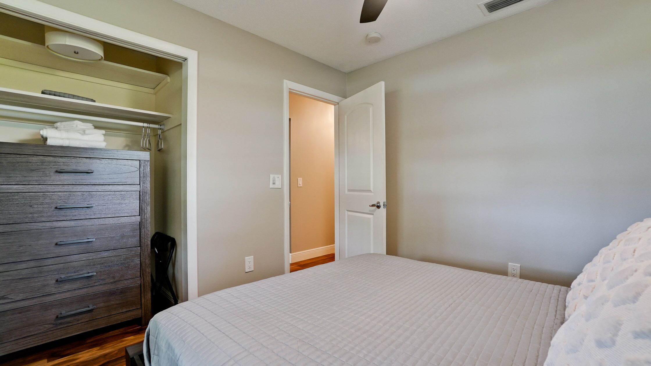 A bedroom with a bed, a dresser, and a door leading to another room.